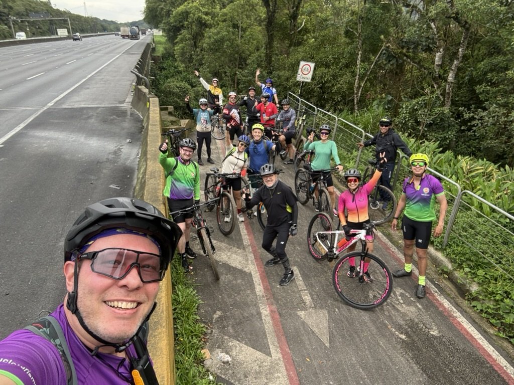 Ciclistas com suas bicicletas em caminho ao lado da rodovia e da mata
